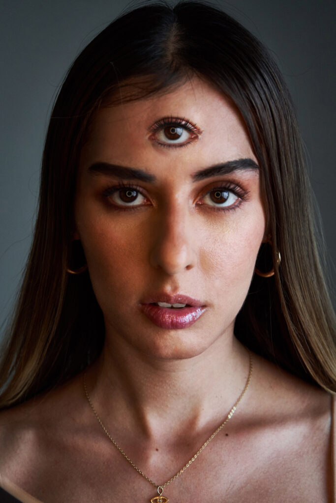 Marintia Bustos portrays a mesmerizing portrait with a unique eye on her forehead gold hoop earrings and a delicate necklace.